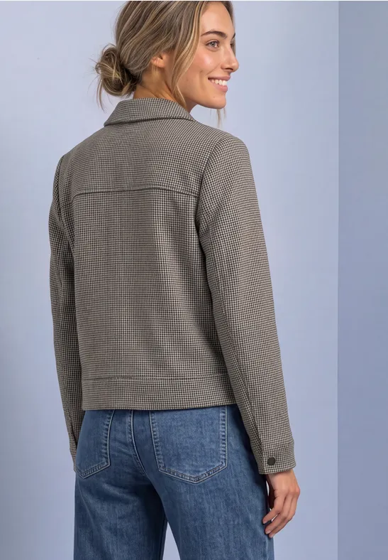 Rückansicht einer Frau in grauer Jacke und blauen Jeans, die lächelnd nach rechts blickt.