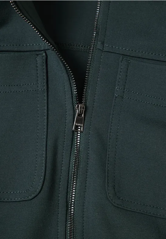 Nahaufnahme eines dunklen Kleidungsstücks mit Reißverschluss und zwei aufgesetzten Taschen.