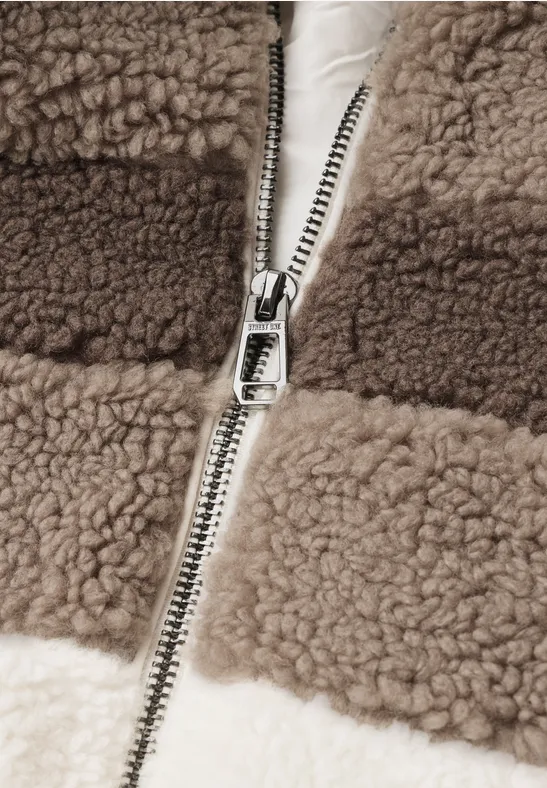 Nahaufnahme eines Reißverschlusses an einer braun-weißen Teddy-Fleecejacke.