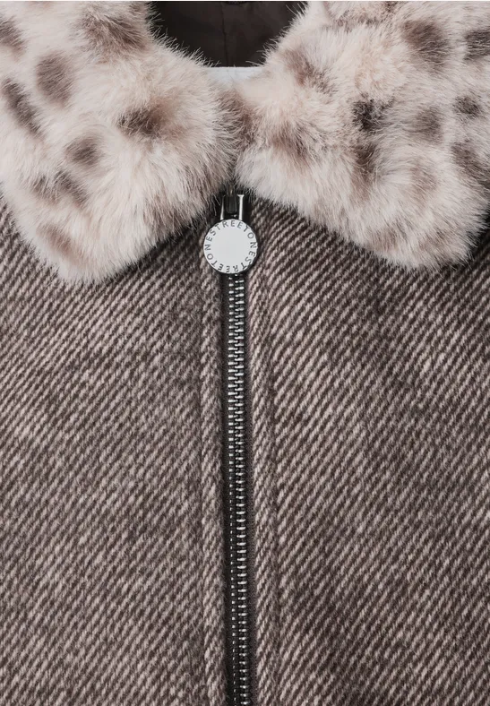 Nahaufnahme eines braunen Tweed-Mantels mit Reißverschluss und einem gepunkteten Fellkragen.