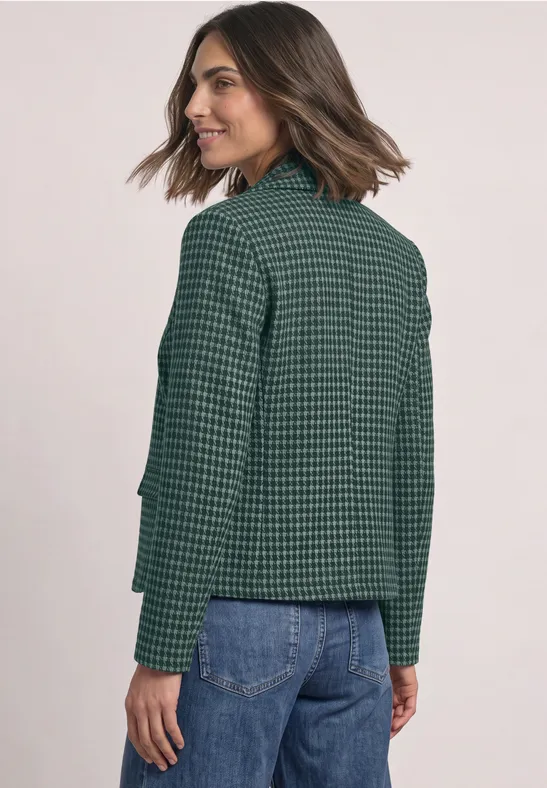 Une femme en veste verte à carreaux et jean bleu regarde par-dessus son épaule.