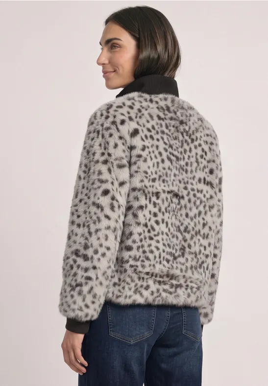 Frau in grauer Kunstfelljacke mit schwarzem Kragen und Leopardenmuster, seitlich stehend.