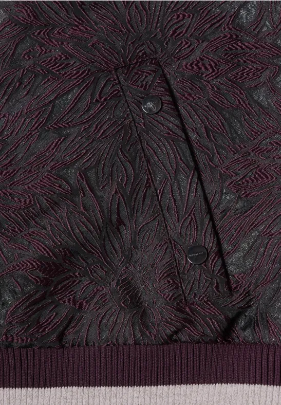 Dunkellila Jacke mit organischem, reliefartigem Muster, sichtbaren Knöpfen und geripptem Saum.