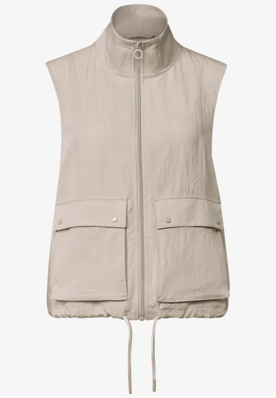Beige mouwloze bodywarmer met opstaande kraag, ritssluiting, klepzakken en verstelbare zoom.