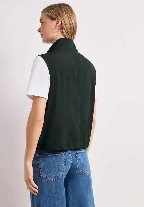 Achteraanzicht van een persoon met een zwart gilet, een wit T-shirt en een blauwe spijkerbroek.