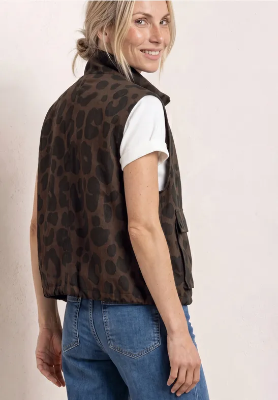 Vrouw zijwaarts gekeerd in wit T-shirt, blauwe jeans en mouwloos bruin luipaardprint gilet