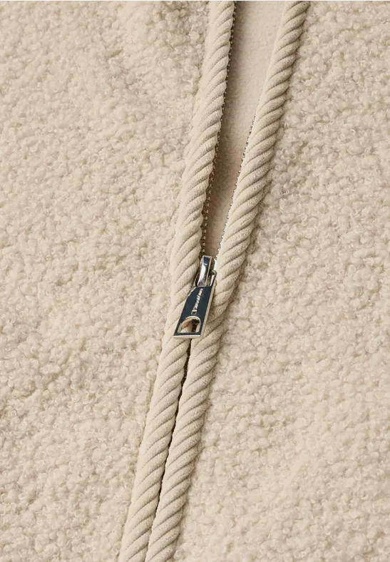 Nahaufnahme eines beigen Teddy-Fleece-Oberteils mit Reißverschluss und Kordelzug.