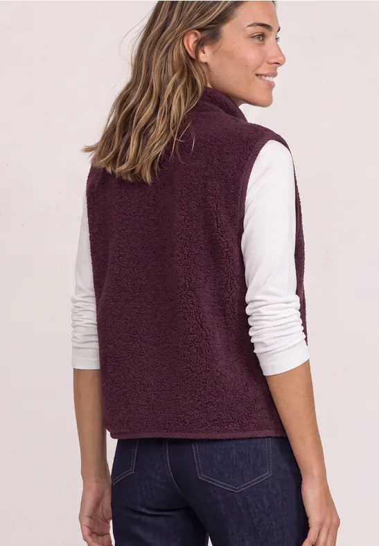 Frau von hinten in weißem Langarmshirt und dunkelroter Fleece-Weste, blickt nach links.