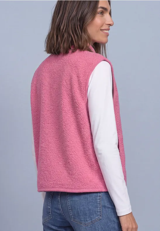 Vrouw van achteren in een roze teddyvest met een wit shirt met lange mouwen en een blauwe spijkerbroek.
