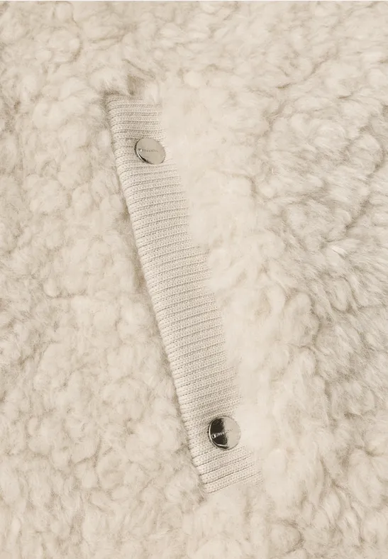 Gros plan d’un tissu polaire crème et duveteux avec une sangle cousue et deux boutons-pression métalliques.