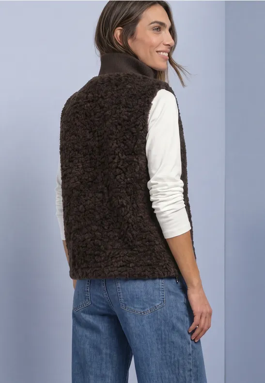 Femme vue de dos portant une veste polaire marron, un haut blanc à manches longues et un jean bleu