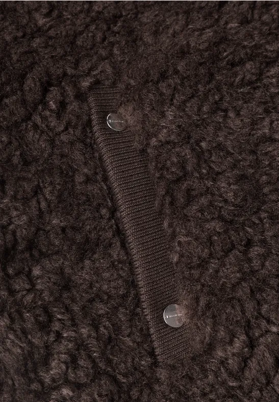 Gros plan d’un manteau en fausse fourrure marron foncé avec poche et pressions argentées.