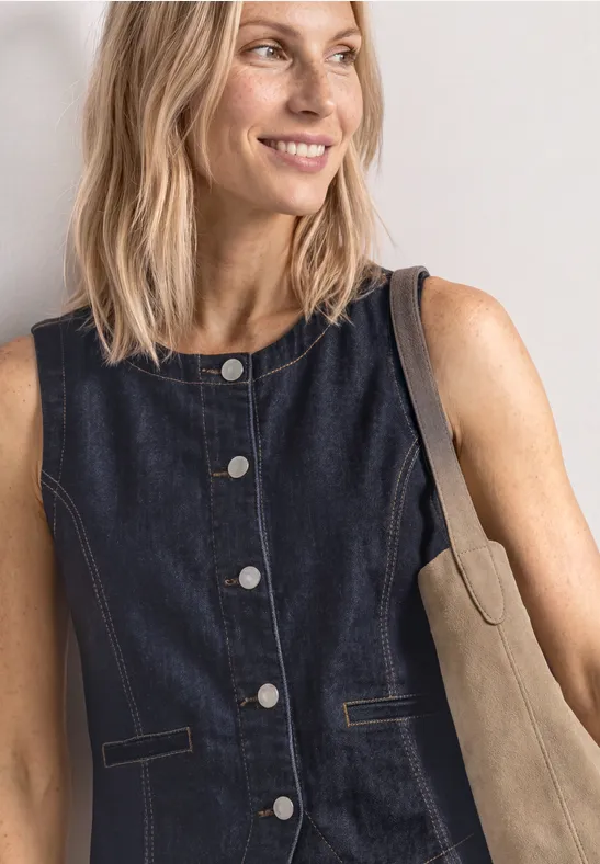 Vrouw met mouwloos denimgilet in donkerblauw en beige schoudertas voor lichte achtergrond.