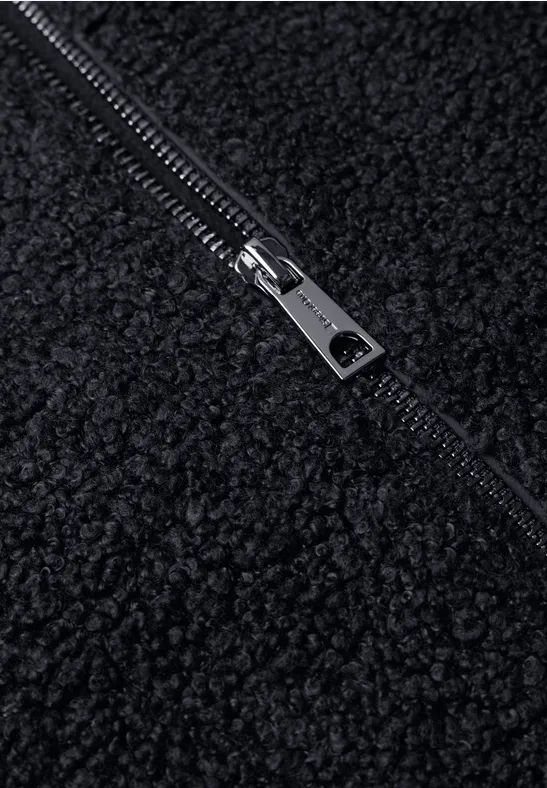 Close-up van een zwarte teddyfleece-stof met een zilverkleurige metalen rits.