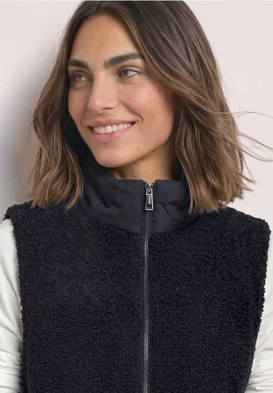 Vrouw met zwarte teddy-fleece bodywarmer met rits en opstaande kraag, glimlachend opzij.