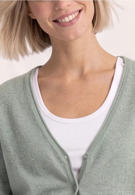 Frau trägt hellgrünen Cardigan über weißem Top, lächelt leicht.