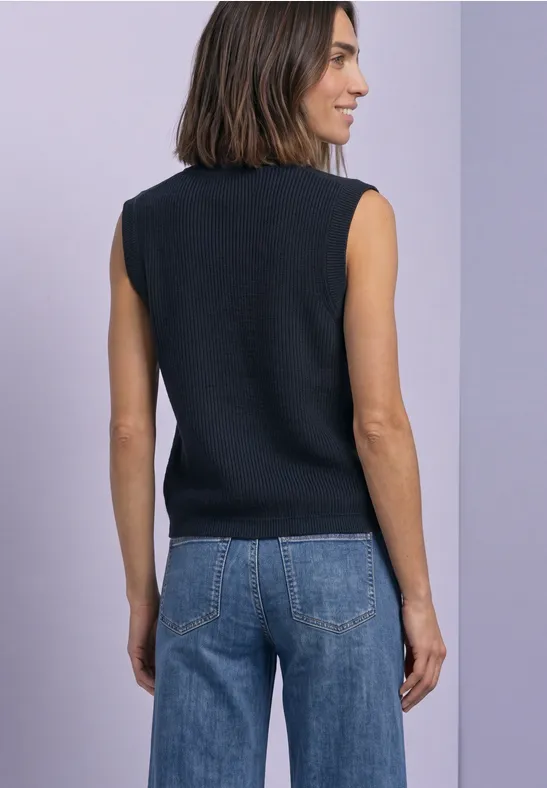 Eine Frau von hinten in ärmellosem schwarzem Top und Jeans vor hellem Hintergrund.
