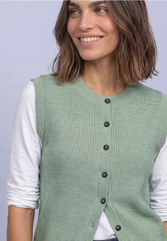 Lächelnde Frau in hellgrüner Strickweste und weißem Langarmshirt