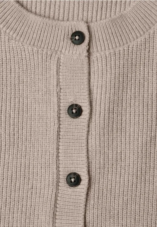 Beige Strickjacke mit Rippenbündchen und drei dunklen Kunststoffknöpfen mittig.