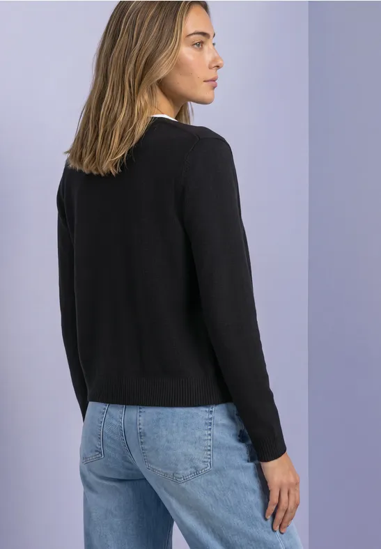 Frau im Profil, schwarzer Pullover, blaue Jeans, vor lila Hintergrund.