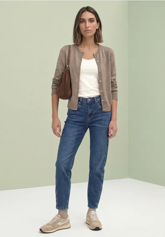 Vrouw met bruin vest, wit topje, blauwe jeans, sneakers en bruine tas