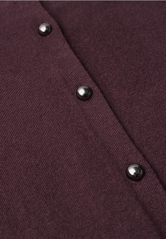 Nahaufnahme eines dunkelroten Strickstoffs mit drei schwarzen Knöpfen.