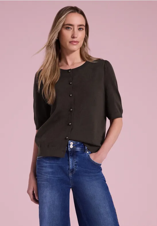 Frau vor rosa Hintergrund in schwarzer Bluse mit Knöpfen und blauen Jeans