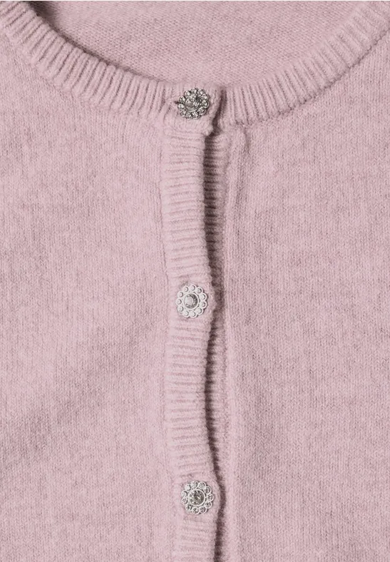 Nahaufnahme eines rosa Strickcardigans mit Rippenbündchen und funkelnden Schmuckknöpfen.