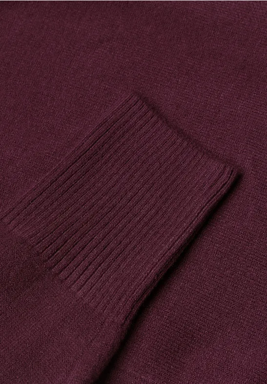 Nahaufnahme eines weinroten Strickpulloverärmels mit Rippenstrickbündchen.