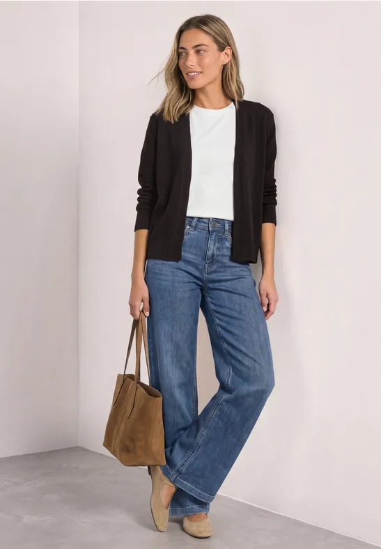 Frau in weißem T-Shirt, schwarzer Jacke, weiten Jeans, beigen Schuhen und brauner Tasche