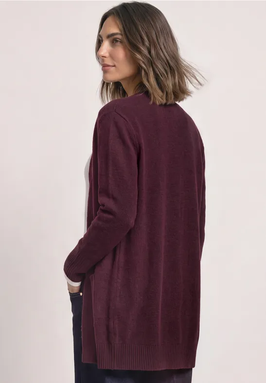 Femme de profil portant un long cardigan bordeaux, regard tourné sur le côté.