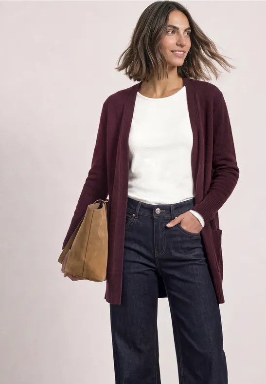 Femme en gilet bordeaux, t-shirt blanc, jean foncé et sac beige, sourire naturel, allure décontractée.