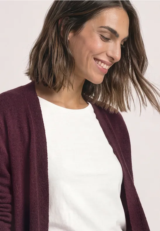 Une femme souriante en t-shirt blanc et gilet bordeaux.