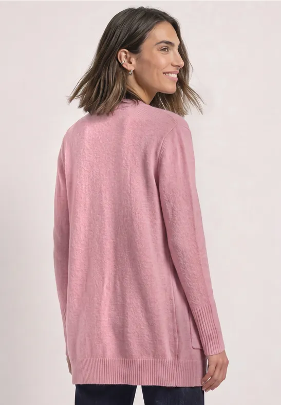 Frau trägt langen rosa Strickcardigan mit Taschen vor hellem Hintergrund.