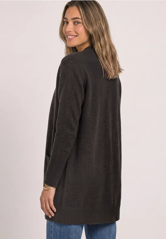 Jeune femme de profil portant un long cardigan marron foncé et souriant à la caméra.