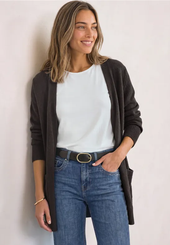 Femme souriante en t-shirt blanc, cardigan foncé et jean avec ceinture.