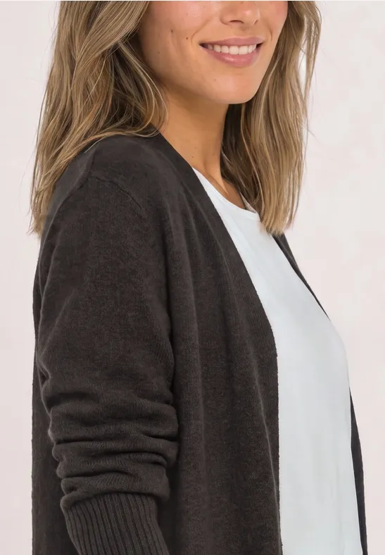 Femme souriante en gilet marron foncé sur un t-shirt blanc, photographiée de côté.