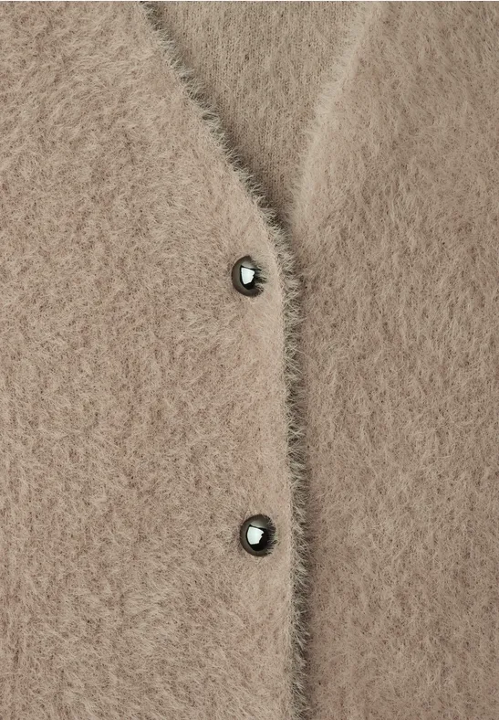 Beige Fluffy-Strickjacke mit zwei dunklen Knöpfen aus wolligem Material.