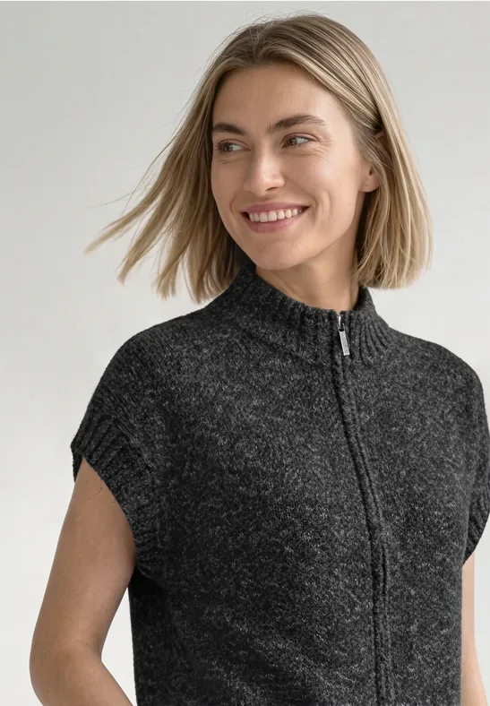 Eine lächelnde Frau trägt einen kurzen, dunkelgrauen Strickpullover mit Stehkragen und Reißverschluss.