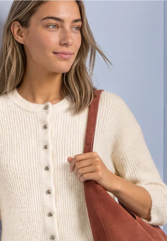 Junge Frau in cremefarbener Strickjacke mit Knöpfen trägt eine rostrote Umhängetasche.