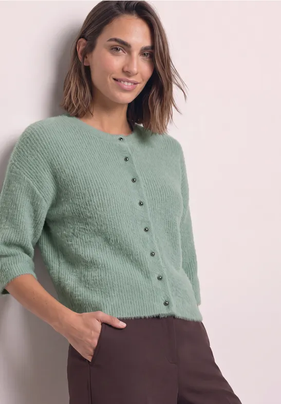 Frau in mintgrünem Kurzarm-Cardigan mit Knopfleiste und brauner Hose, Hand in Tasche