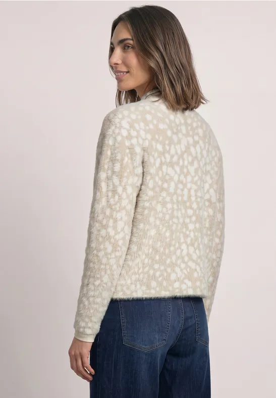 Frau steht im Profil, trägt gemusterten Creme-Pullover und blaue Jeans.