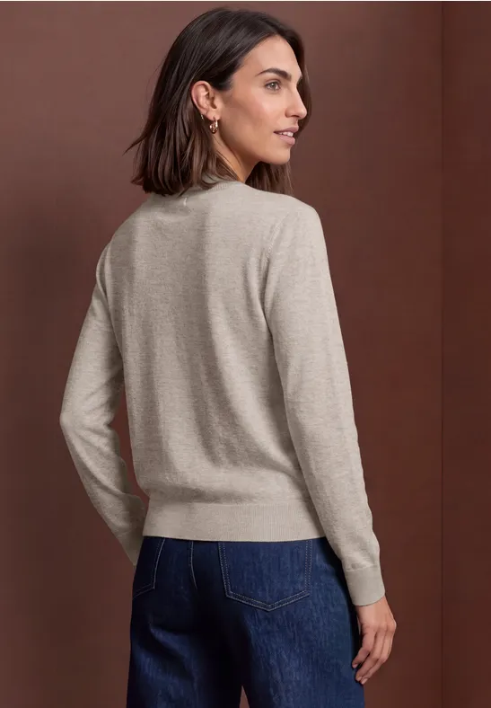 Frau in beigem Pullover und blauen Jeans, von hinten vor braunem Hintergrund