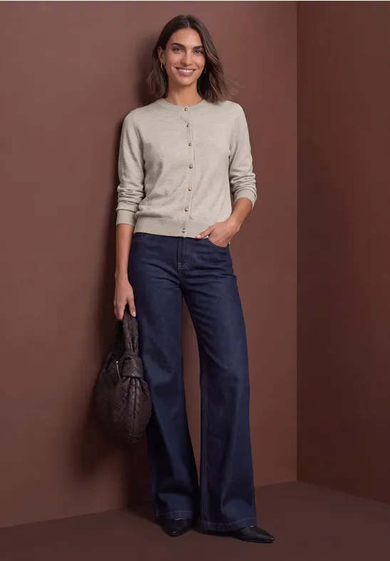 Frau trägt beigefarbenen Cardigan und weite dunkelblaue Jeans, sie hält eine schwarze Handtasche.