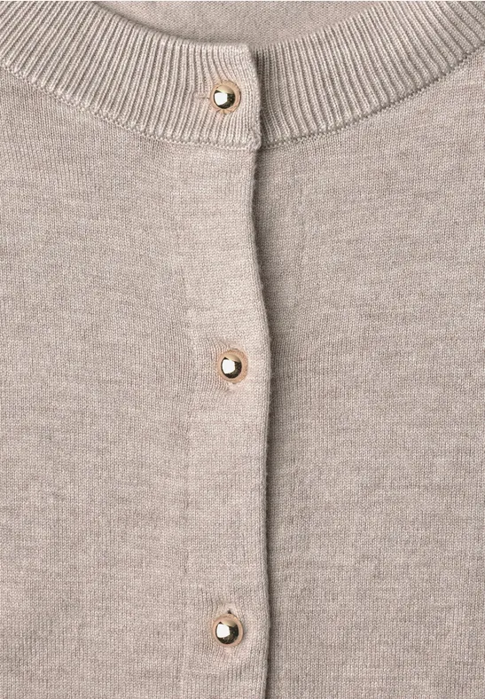 Nahaufnahme eines beigen Strickcardigans mit goldenen Perlenknöpfen.