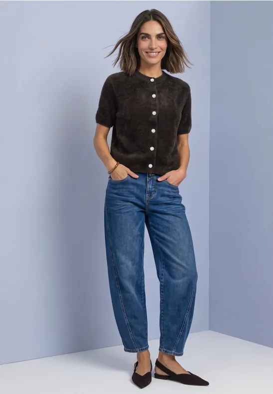 Vrouw in bruine korte blouse, wijde spijkerbroek en puntige schoenen voor lila achtergrond.