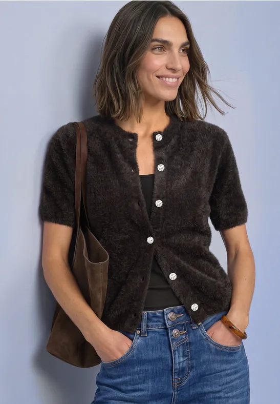 Vrouw in een korte, donzige bruine cardigan op een zwart topje, blauwe jeans en een bruine schoudertas