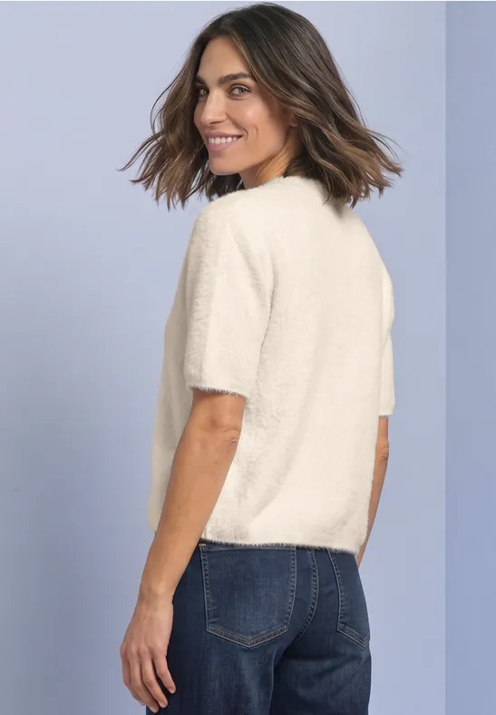 Femme en t-shirt clair et jean bleu, regard par-dessus l'épaule, sourire aux lèvres.