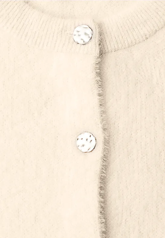 Gilet tricoté beige doux, bordure effilochée subtile et deux gros boutons effet marbré.