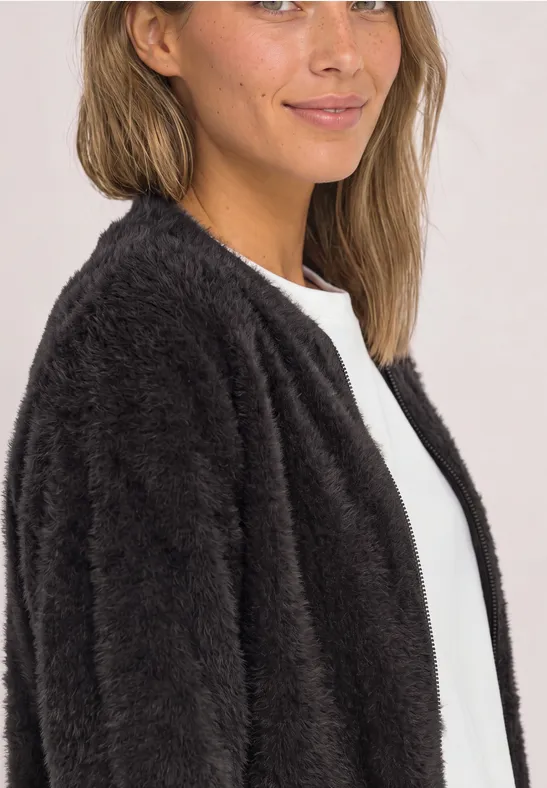Eine Frau trägt eine flauschige schwarze Jacke aus Teddy-Fleece und ein weißes Oberteil.